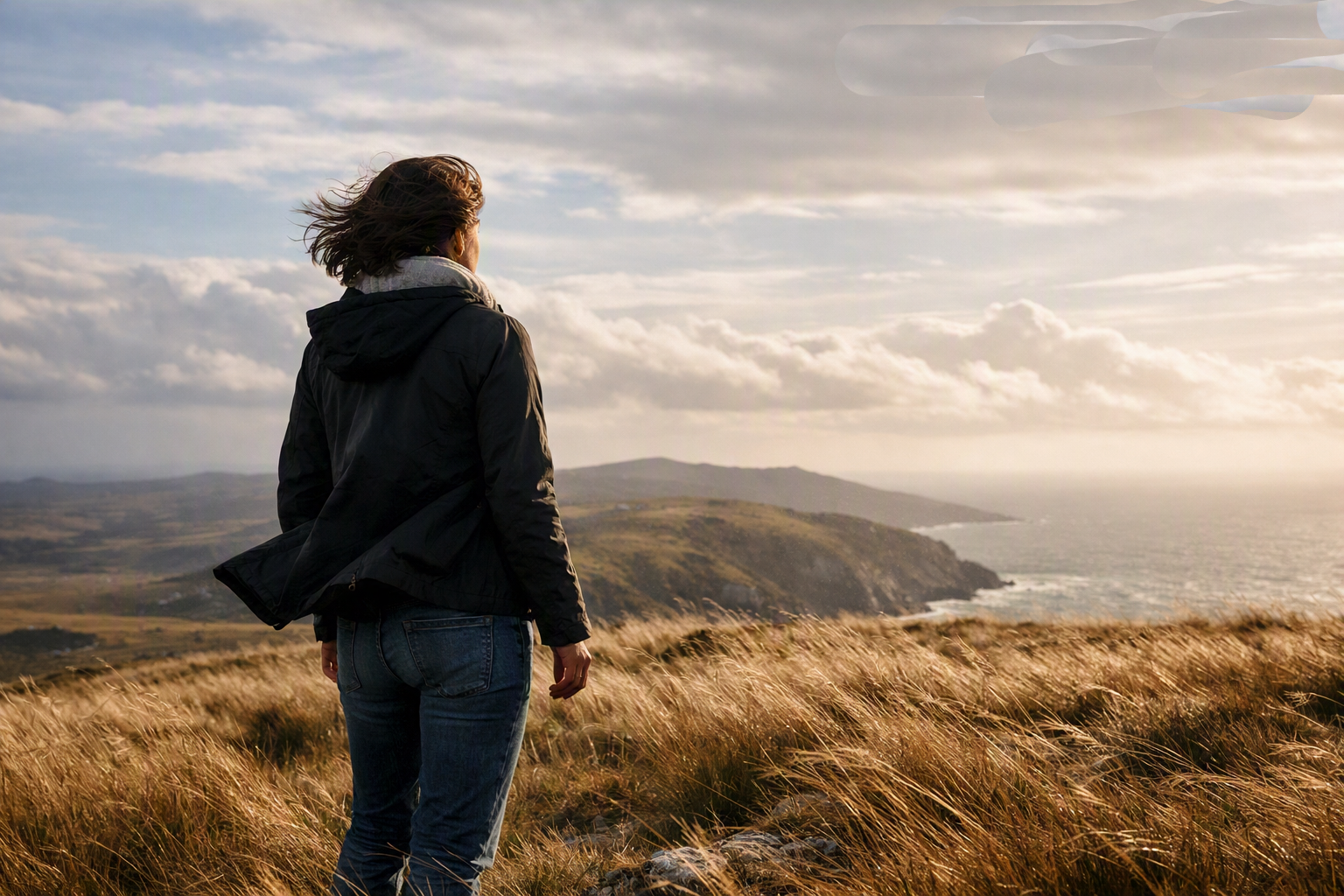 Eine Person steht auf einer windigen Küstenlandschaft und blickt in die offene Weite. Der Wind bewegt Kleidung und Haare – ein Bild für Freiheit und die befreiende Kraft des göttlichen Rufes.